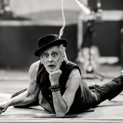 Das schwarz-weiß Bild zeigt Melingo, wie er auf dem Bauch liegt und seinen Kopf auf dem linken arm abstützt. Seine Augen sind weit aufgerissen und er trägt einen Hut.